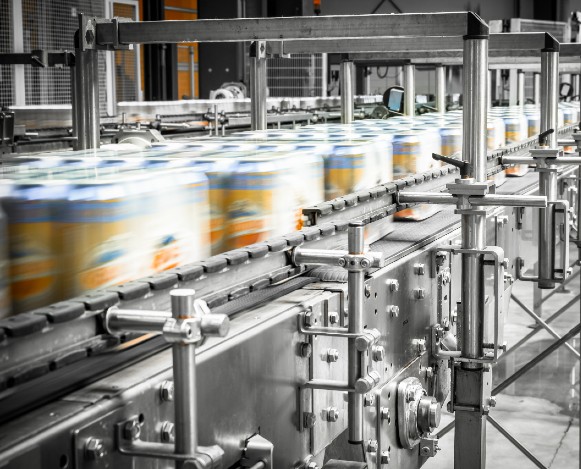 Line of beverage cans go by quickly on a conveyor belt in a canning facility.